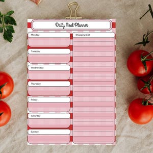 May include: A Daily Meal Planner notepad with a red and white striped border and a gold clip. The notepad has sections for each day of the week and a shopping list. The title "Daily Meal Planner" is printed at the top.