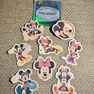 May include: A selection of Mickey and Minnie Mouse stickers in different poses, alongside a holographic bag with the text "You have been PIXIE DUSTED by the Wooler Family". The stickers showcase the characters in bright colours and designs.