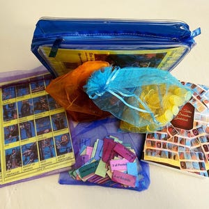 May include: A collection of tarot-related items, including a blue zippered case, several small mesh bags, and a guidebook. The mesh bags contain items like gold coins, tarot cards, and small rectangular cards with text. The guidebook has a colorful mosaic design.