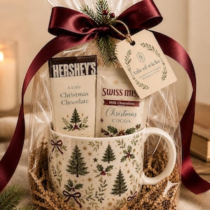 May include: A gift set in clear cellophane with a dark red satin ribbon and a tag reading tale of wicks. It contains a white mug with a green Christmas tree and holly pattern, a Hershey's Christmas chocolate bar, and a packet of Swiss Miss cocoa.