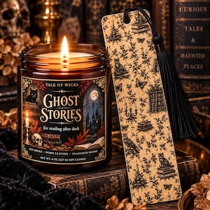 May include: An 8 oz soy candle in an amber glass jar with a label reading Tale of Wicks Ghost Stories for reading after dark, featuring a lit wick, and a rectangular bookmark with a black tassel and a pattern of cats, butterflies, and books.