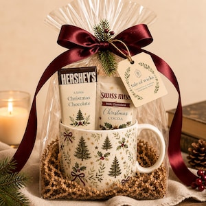 Heritage Christmas mug gift set with coordinating wrapped Hershey’s chocolate and Swiss Miss cocoa, presented in clear cello with kraft paper shred, burgundy satin ribbon, evergreen accent and Tale of Wicks gift tag.