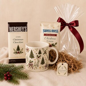 Alt text: Heritage Christmas mug gift set contents with vintage evergreen and holly mug, full-size Hershey’s chocolate and Swiss Miss cocoa in coordinating Christmas sleeves, clear cello bag, burgundy ribbon, kraft paper shred and Tale of Wicks gift tag