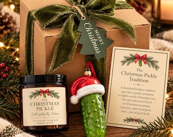 May include: A brown gift box with a green velvet ribbon and a tree-shaped tag reading Merry Christmas. Includes a candle labeled The Christmas Pickle, a green pickle ornament wearing a Santa hat, and a card explaining The Christmas Pickle Tradition.