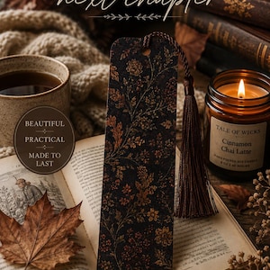 Moody autumn botanical bookmark with brown tassel featured in a cozy fall reading scene with vintage books, warm tea, glowing candle, knit blanket and autumn leaves, styled as a gift for book lovers.