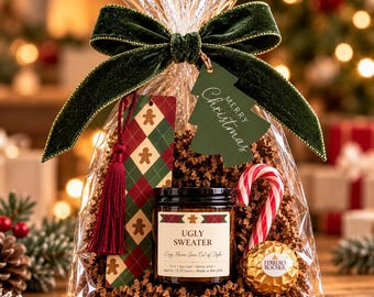 May include: A clear gift bag containing a candle labeled Ugly Sweater, a candy cane, a Ferrero Rocher chocolate, and a gingerbread-patterned bookmark with a tassel. The bag is tied with a dark green velvet ribbon and a tree-shaped Merry Christmas tag.