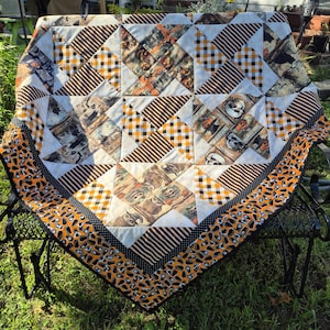 May include: A square quilt featuring a pinwheel pattern with alternating blocks of orange and black plaid, black and white stripes, and fabric printed with skulls, pumpkins, and owls. The quilt has a wide border with a black and orange candy corn print.