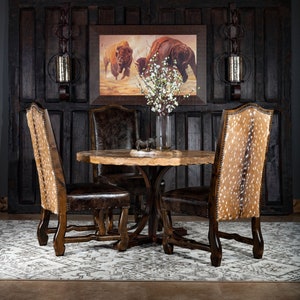 May include: A rustic dining set featuring a round wooden table and four chairs. The chairs have brown leather seats and backs with a spotted pattern. A framed painting of bison hangs on a dark wood paneled wall.