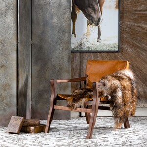 May include: A brown leather armchair with a faux fur throw draped over the back. The chair is in front of a wall with a framed print of a brown horse.