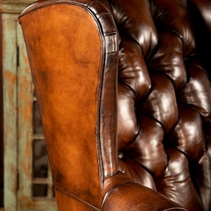May include: A brown leather wingback chair with button tufting. The chair has a high back and a deep seat.