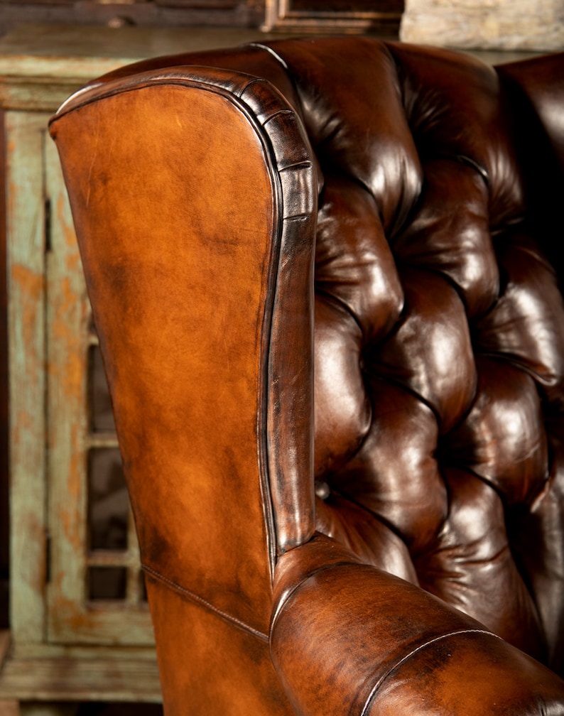 May include: A brown leather wingback chair with button tufting. The chair has a high back and a deep seat.