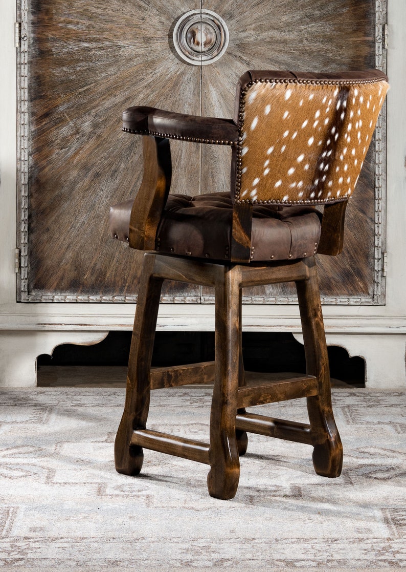 May include: A brown wooden bar stool with a brown leather seat and a back upholstered in spotted cowhide. The stool has a swivel base and a footrest.