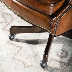 May include: A brown leather office chair with a swivel base and five caster wheels. The chair has a tufted back and a decorative nailhead trim.