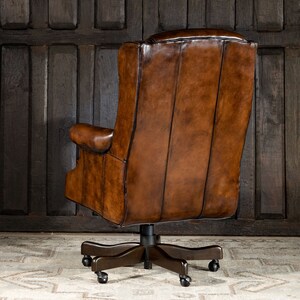May include: A brown leather office chair with a high back and a swivel base. The chair has a tufted back and a padded seat. The chair is on a light brown rug.