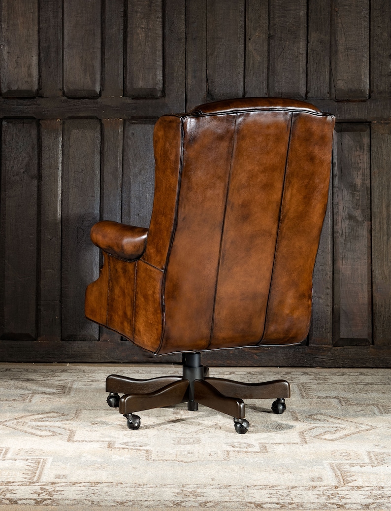 May include: A brown leather office chair with a high back and a swivel base. The chair has a tufted back and a padded seat. The chair is on a light brown rug.