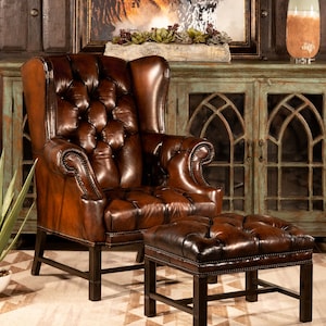 May include: A brown leather armchair with a tufted back and seat, and a matching brown leather ottoman. The chair and ottoman are in front of a wooden cabinet with glass doors.