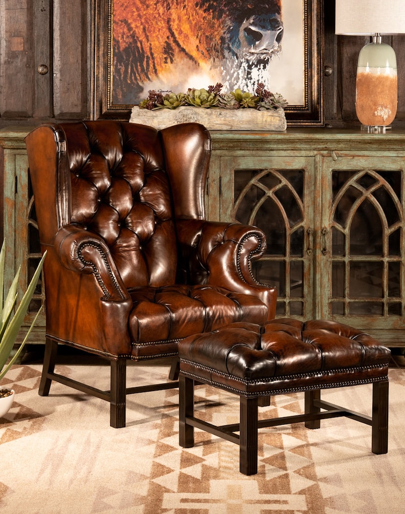 May include: A brown leather armchair with a tufted back and seat, and a matching brown leather ottoman. The chair and ottoman are in front of a wooden cabinet with glass doors.