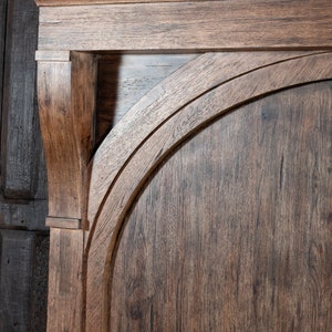 May include: Close-up of a wooden door with an arched top. The wood is a dark brown color and has a rustic finish.
