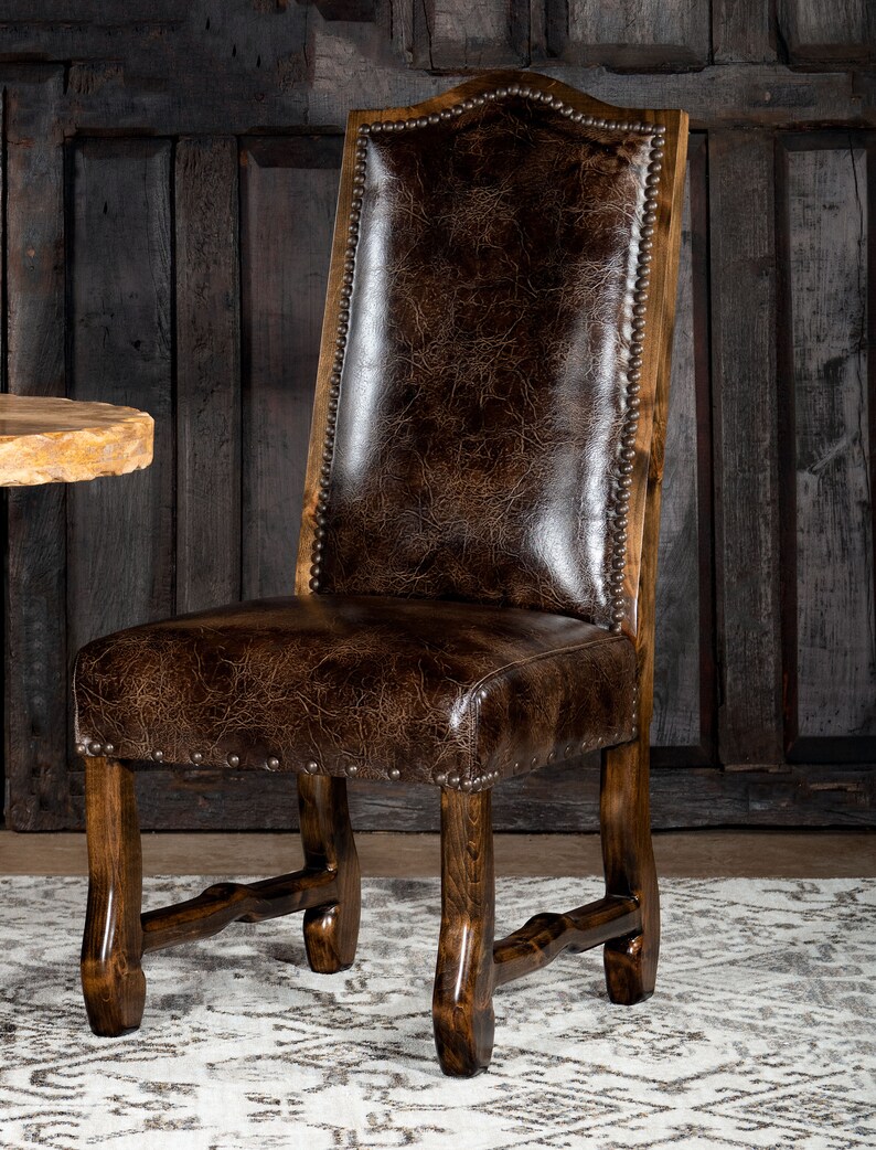 May include: A dark brown leather chair with a wooden frame. The chair has a high back and a padded seat. The leather is distressed, and the frame is a dark wood. The chair is accented with metal studs.