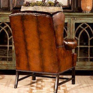 May include: A brown leather wingback chair with a tufted back and a dark brown wood frame. The chair is sitting on a rug with a geometric pattern.