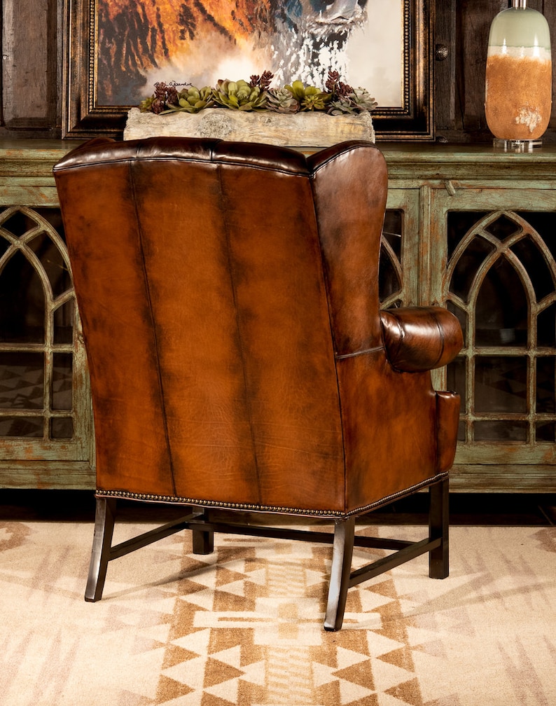 May include: A brown leather wingback chair with a tufted back and a dark brown wood frame. The chair is sitting on a rug with a geometric pattern.