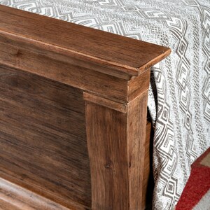 May include: Close-up of a wooden bed frame with a decorative molding detail. The frame is a rich brown color and has a smooth finish.