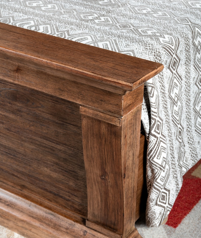 May include: Close-up of a wooden bed frame with a decorative molding detail. The frame is a rich brown color and has a smooth finish.