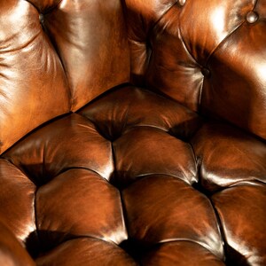 May include: Close-up of a brown leather armchair with a tufted seat and back. The leather is worn and has a rich patina.