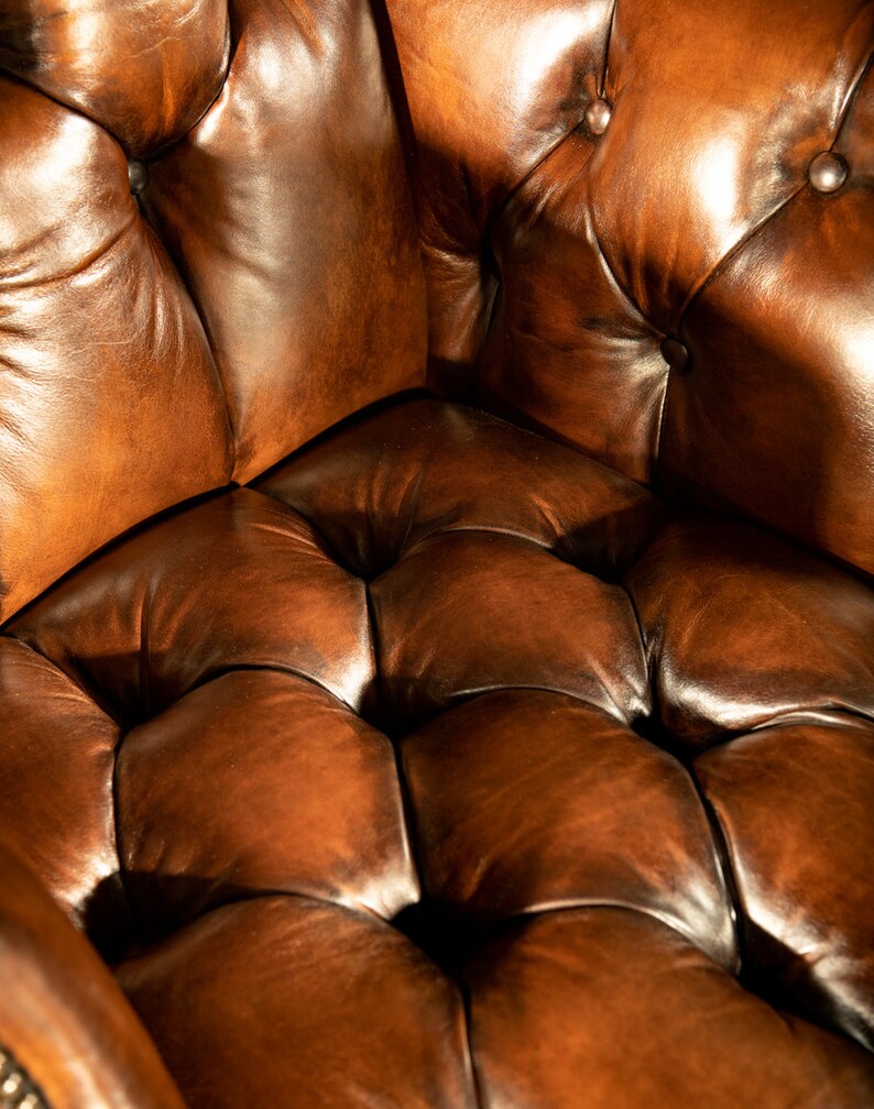 May include: Close-up of a brown leather armchair with a tufted seat and back. The leather is worn and has a rich patina.