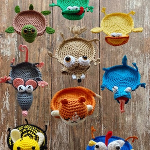 Può includere: Una collezione di nove sottobicchieri all'uncinetto a forma di animale, tra cui una rana verde, una tartaruga rosa, un'anatra gialla, un topo grigio, una creatura beige, un uccello blu, un'ape, un gatto arancione e un pollo blu.
