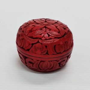 May include: A spherical, red decorative box with detailed floral carvings. The box is a deep red colour and features intricate carvings of flowers and leaves. The box is a sphere shape.