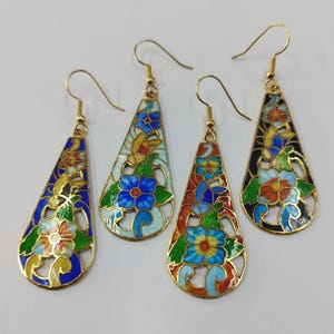 Puede incluir: Tres pares de pendientes colgantes con forma de lágrima. Cada pendiente tiene un marco de metal dorado con un diseño de esmalte colorido de flores y hojas. Los pendientes están disponibles en azul, rojo y blanco.