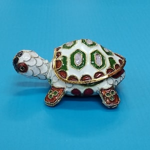 May include: A small, white turtle figurine with green, red, and gold accents. The turtle's shell is decorated with a geometric pattern.