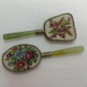 Könnte beinhalten: Zwei antike Handspiegel mit Blumenstickerei auf der Vorderseite. Die Spiegel haben jadegrüne Griffe mit silbernen Akzenten.