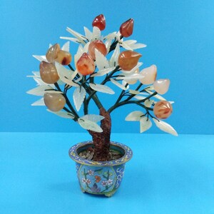May include: A jade tree with peach-shaped agate stones in a blue and white cloisonné pot. The tree is made of jade and the pot is decorated with flowers and butterflies.