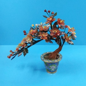 May include: A jade bonsai tree with orange and red flowers in a blue and gold pot. The tree is made of jade and the flowers are made of glass.