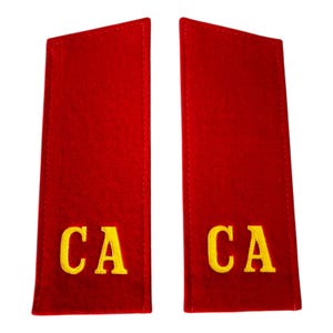 May include: Two red shoulder boards with yellow embroidered letters "CA". The boards are rectangular with rounded top corners and a stitched border. The letters are in a bold, sans-serif font.
