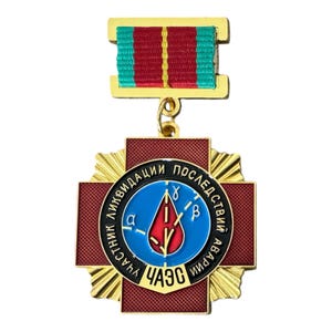 Könnte beinhalten: Eine goldfarbene Metallmedaille mit einem roten Kreuzhintergrund und einem zentralen blauen runden Emblem. Das Emblem zeigt einen roten Tropfen, griechische Buchstaben und kyrillischen Text. Es ist an einer rot-grün-gelb gestreiften Bandschnalle befestigt.