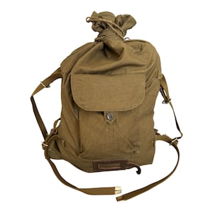 May include: Olive green canvas backpack with a drawstring closure at the top. Features a front flap pocket with a button closure and adjustable shoulder straps. Includes a small leather patch and metal hardware.