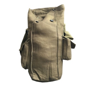 Pu&ograve; includere: Una borsa per maschera antigas in tela verde con due tasche laterali e una chiusura a bottone.