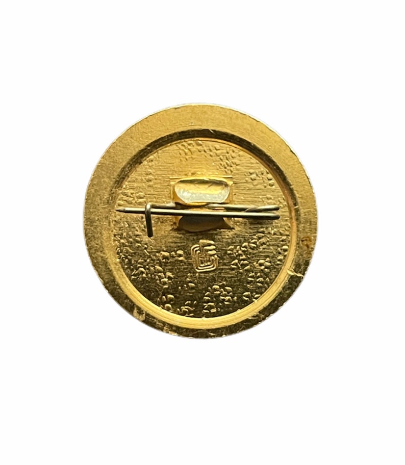 Puede incluir: La parte posterior de un pin redondo de color dorado con un cierre de pin y una peque&ntilde;a inscripci&oacute;n.
