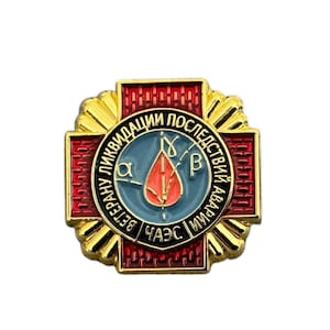 May include: A gold and red enamel pin with a cross design. The center of the pin features a blue circle with a red drop of blood and a stylized leaf. The text around the circle reads "Ветеран ликвидации последствий аварии ЧАЭС".