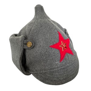 Op de afbeelding: Een grijze Ushanka-muts met oorflappen en een rood ster-embleem. De hoed heeft een knoopsluiting en een puntige kroon. De rode ster heeft een gouden hamer- en sikkel-embleem.