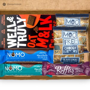 May include: An open cardboard box filled with various chocolate bars and snacks. The box contains two chocolate bars from the brand "Well & Truly", two chocolate bars from the brand "Nomo", a chocolate bar from the brand "Oat M&LK", two bags of chocolate buttons from the brand "Moo Free", and a chocolate bar from the brand "Ruffles".