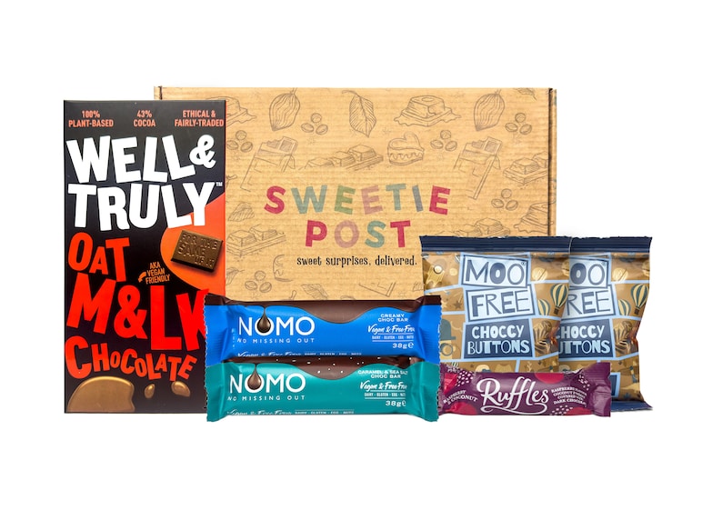 May include: A brown cardboard box with the words "Sweetie Post" printed on it. The box contains a variety of chocolate bars and snacks, including Well & Truly Oat M&L Chocolate, Moo Free Choccy Buttons, and NomO Vegan & Free From Chocolate Bars.
