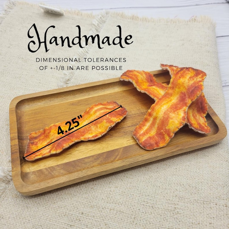 Op de afbeelding: Handgemaakte spekstrips, elk ongeveer 10,8 cm lang, zijn gerangschikt op een houten dienblad. Het spek heeft een realistisch ontwerp met rode en gele tinten. De tekst "Handmade" en informatie over de maattolerantie zijn zichtbaar.