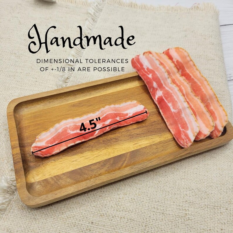 Op de afbeelding: Handgemaakte spekstrips, &eacute;&eacute;n van 11,4 cm, liggen op een houten dienblad. Het spek is een mix van roze en rood met witte marmering, die de look van gebakken spek imiteert. De lade ligt op een beige stof.