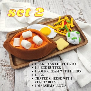 Puede incluir: Un conjunto de alimentos de fieltro en una bandeja de madera, que incluye una batata horneada con malvaviscos, una pieza de mantequilla, crema agria con hierbas, un huevo, queso rallado con verduras y una pieza de pan. El texto "set 2" est&aacute; escrito en amarillo sobre un pa&ntilde;o blanco en el fondo.