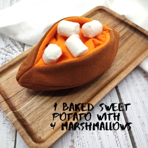 Puede incluir: Una batata asada rellena de cuatro malvaviscos en una bandeja de madera. El texto "1 BAKED SWEET POTATO WITH 4 MARSHMALLOWS" est&aacute; escrito debajo de la bandeja.