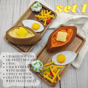 Puede incluir: Conjunto 1 de un juego de comida de fieltro que incluye una patata al horno o una batata, un huevo, crema agria con hierbas, un trozo de mantequilla, queso rallado y verduras. La comida est&aacute; dispuesta en dos bandejas de madera.